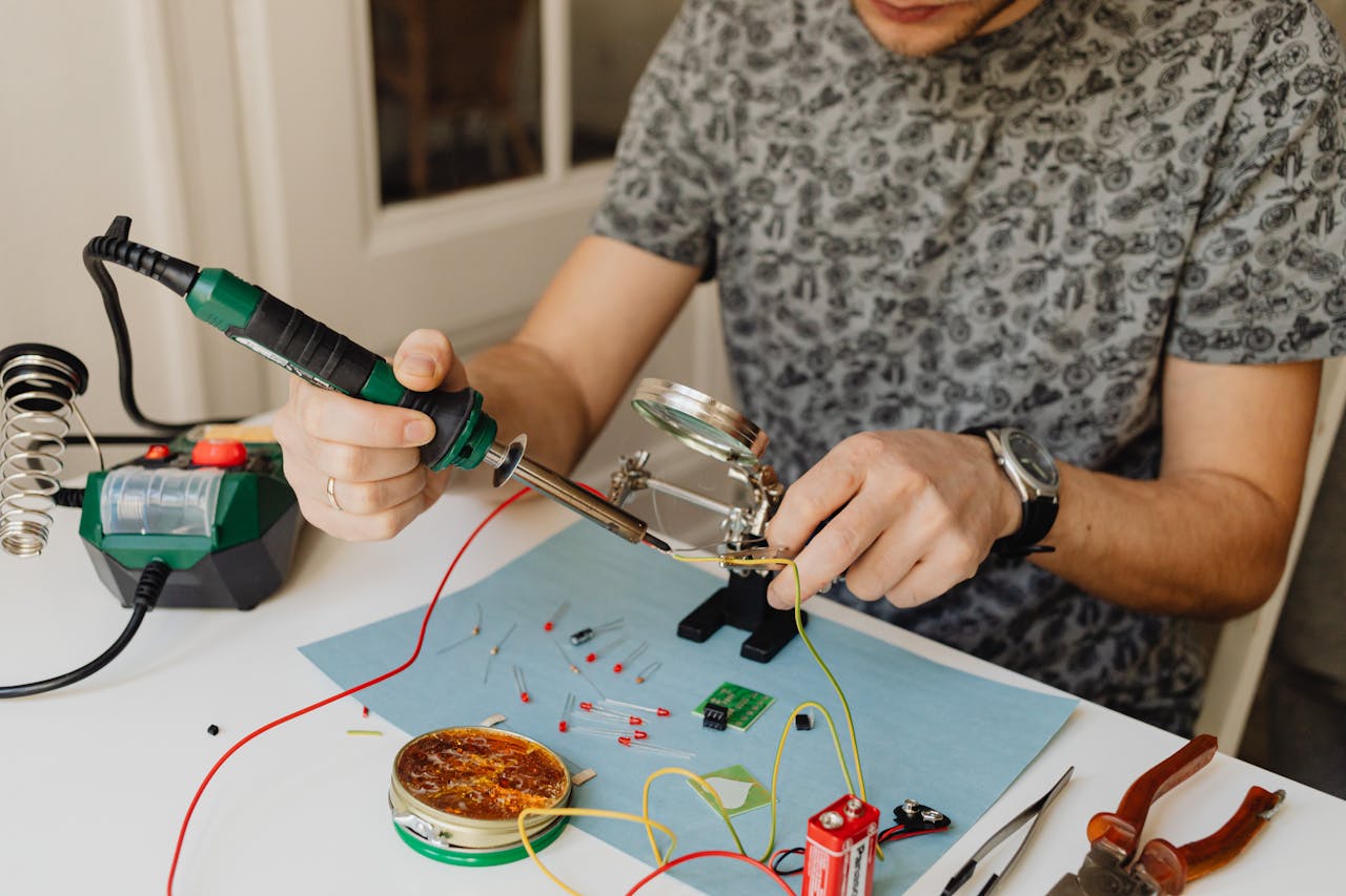 A person soldering electronic components with a soldering iron on a workbench.